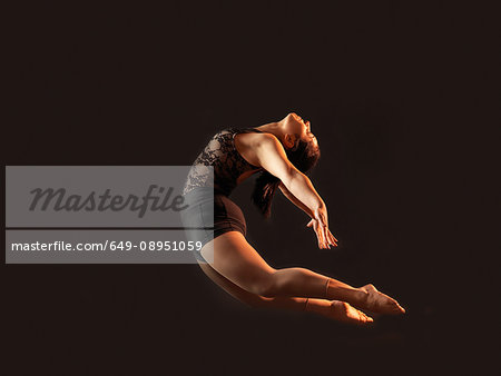 Low key shot of young female dancer bending backwards whilst leaping mid air