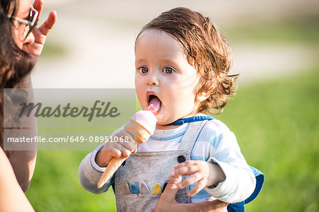 Woman with toddler son eating ice cream cone in park