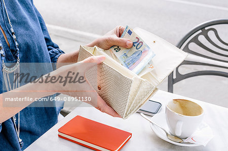 Hand of mature woman removing euro note from purse at sidewalk cafe, Fiesole, Tuscany, Italy