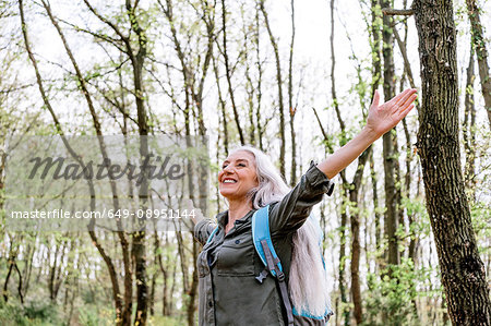 Mature woman with long grey hair with open arms in forest, Scandicci, Tuscany, Italy