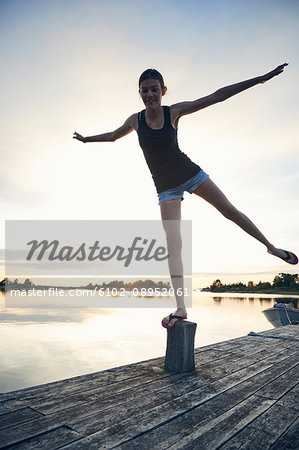 Teenage girl standing on wooden pole by lake