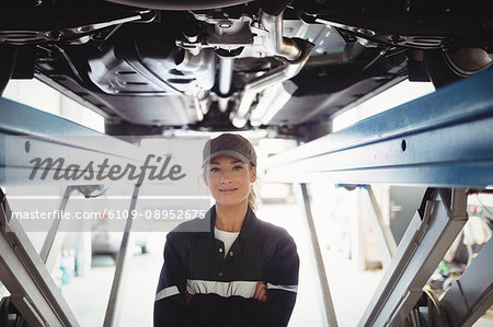 Female mechanic standing with arms crossed under a car Female mechanic standing with arms crossed under a car