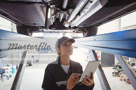Female mechanic using digital tablet under a car Female mechanic using digital tablet under a car