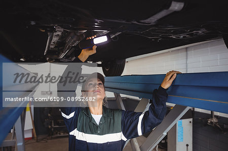 Female mechanic examining a car with flashlight Female mechanic examining a car with flashlight