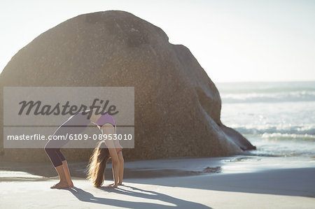 Beautiful woman performing stretching exercise on beach