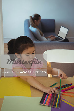 Girl selecting color pencil while mother using laptop in background