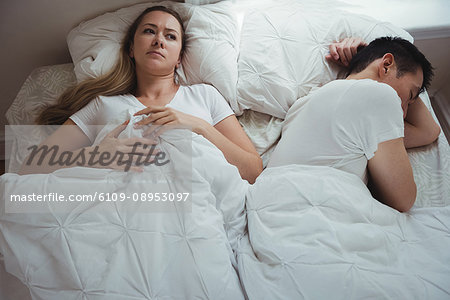 Worried woman lying while man sleeping beside her in bedroom