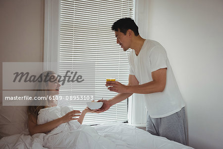 Man serving breakfast to woman in bedroom