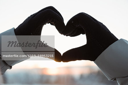 Hand making a heart shape against sunrise