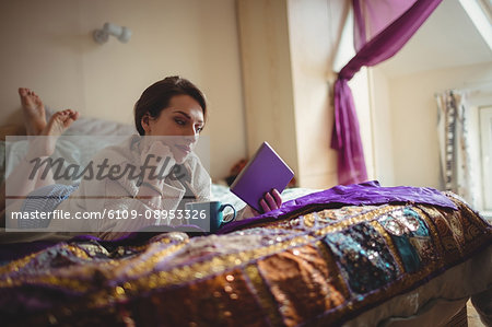 Woman using digital tablet while having coffee on bed