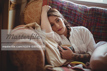 Woman holding coffee cup and lying on sofa