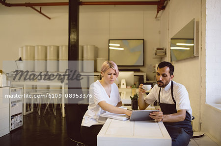 Male and female barista having coffee while using digital tablet in coffee shop