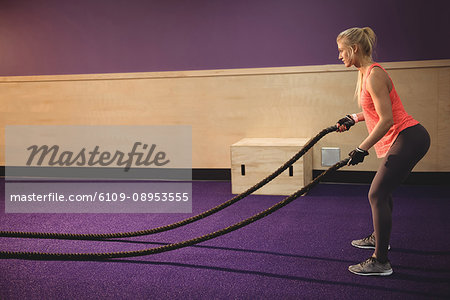 Fit woman doing battle rope exercise in the gym
