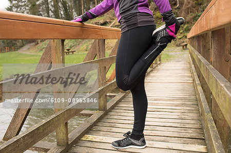 Mid section of woman performing stretching exercise on the bridge in forest
