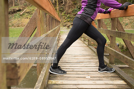 Mid section of woman performing stretching exercise on the bridge in forest