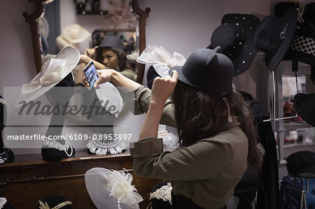 Woman taking selfie while trying hat in jewelry section of boutique