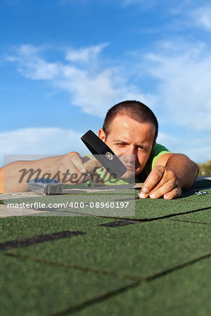 Man fastening bitumen roof shingles with nails and hammer - low angle view, focus on hand
