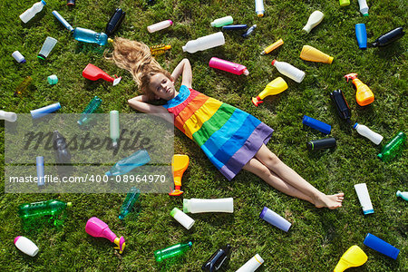 Sad little girl lying on the garbage filled grass - plastic pollution concept