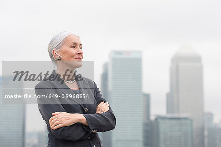 Confident mature businesswoman with arms crossed on city office roof terrace, London, UK