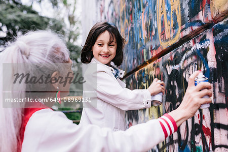 Mature woman and girl spray painting graffiti wall together