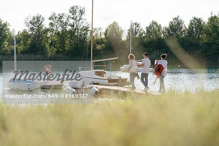 Friends walking towards sailing boat, carrying equipment, long grass in foreground