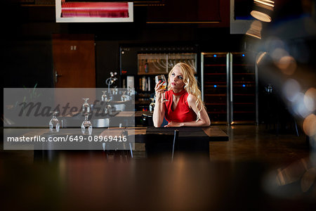 Glamorous young woman with long blond hair sitting alone at restaurant table