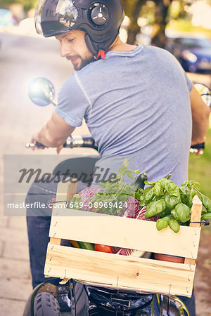 Rear view of man on motorcycling transporting vegetables in crate