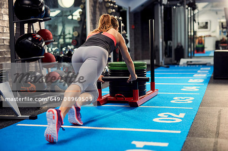 Rear view of young woman training, pushing weight sled in gym