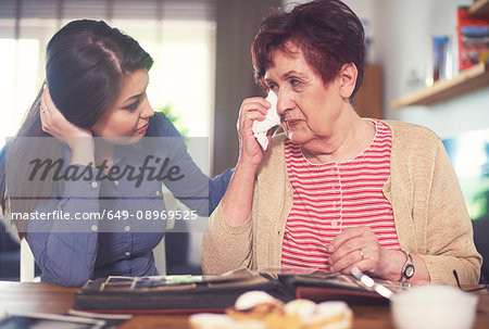 Young woman at table with grandmother crying while looking at photo album