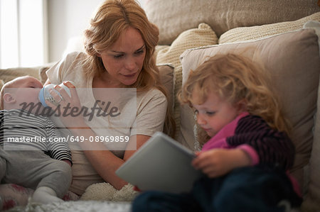 Mother feeding baby son and helping daughter with digital tablet