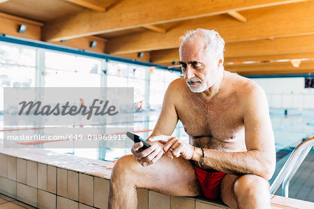 Senior man using mobile phone by edge of swimming pool