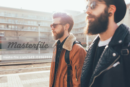 Side view of two young male hipster friends wearing sunglasses in city housing estate