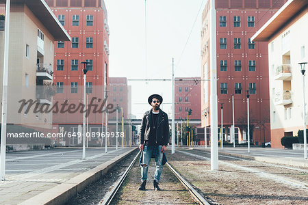 Portrait of young male hipster standing on city tram lines