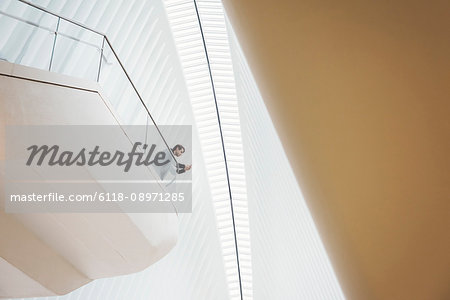 View from below of a man standing on a balcony in the Oculus building looking at his phone. Balconies above the ground in the roof space.