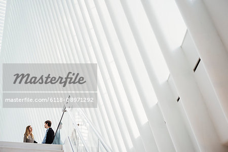 Two people at the top of steps in the central atrium of the Oculus building, talking.