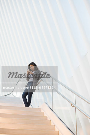 A woman standing on a stairway in the Oculus building at the World Trade Centre under a dramatic ridged white ceiling, checking her phone.