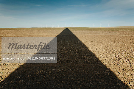 The long black shadow of a wind turbine on the ground, reaching across to the horizon near the Columbia River Gorge in Oregon.