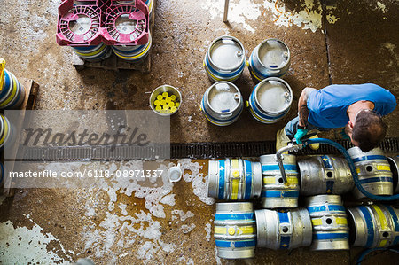 Directly above view of a man working in a brewery, metal beer kegs standing on the floor.