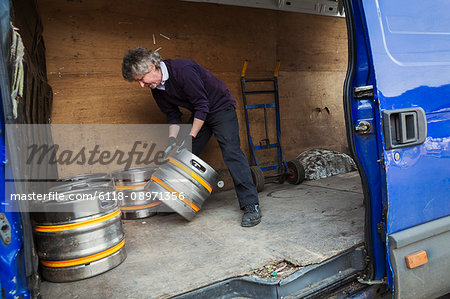 Man working in a brewery, loading metal beer kegs into a van.