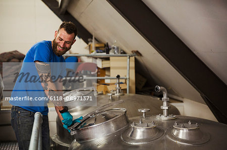 Smiling man working in a brewery, closing lid of a stainless steel tank.