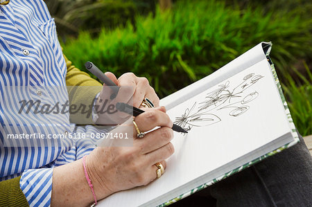 Close up of a woman sitting in a garden, drawing flowers in a sketchbook.