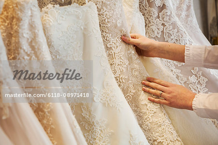 Rows of wedding dresses on display in a specialist wedding dress shop. Close up of full skirts, some with a lace overlay, in a variety of colour tones. .