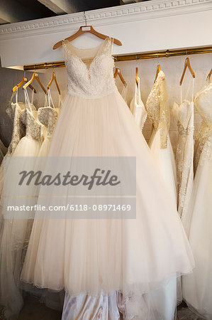 Rows of wedding dresses on display in a specialist wedding dress shop. A white dress on a hanger with a full net skirt.