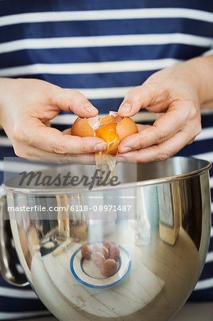 Close up of person wearing a blue and white stripy apron separating egg over a metal bowl.