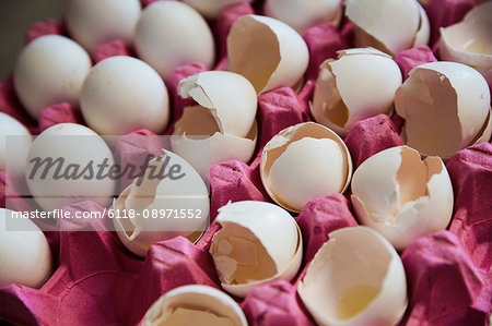 Close up high angle view of white eggs and cracked white egg shells in a pink cardboard tray.