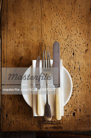 Close up high angle view of plate with knives and fork and a serviette on a rustic wooden table.