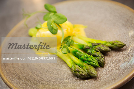 Close up high angle view of green asparagus with Hollandaise sauce and a poached egg on a plate.