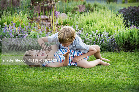 Smiling boy and girl in a garden, roughhousing, playing together, playfighting on a lawn.