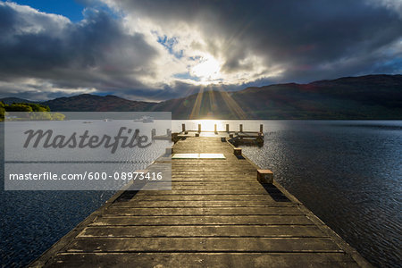 Wooden jetty on lake with dramatic clouds at sunrise at Loch Lomond in Scotland, United Kingdom