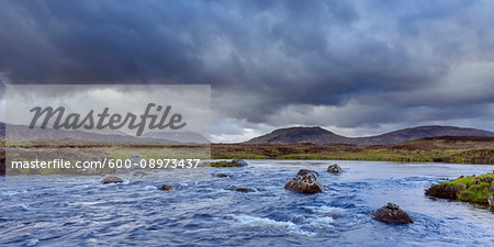 River in moor landscape with dark storm clouds and mountains in the background at Rannoch Moor in Scotland, United Kingdom